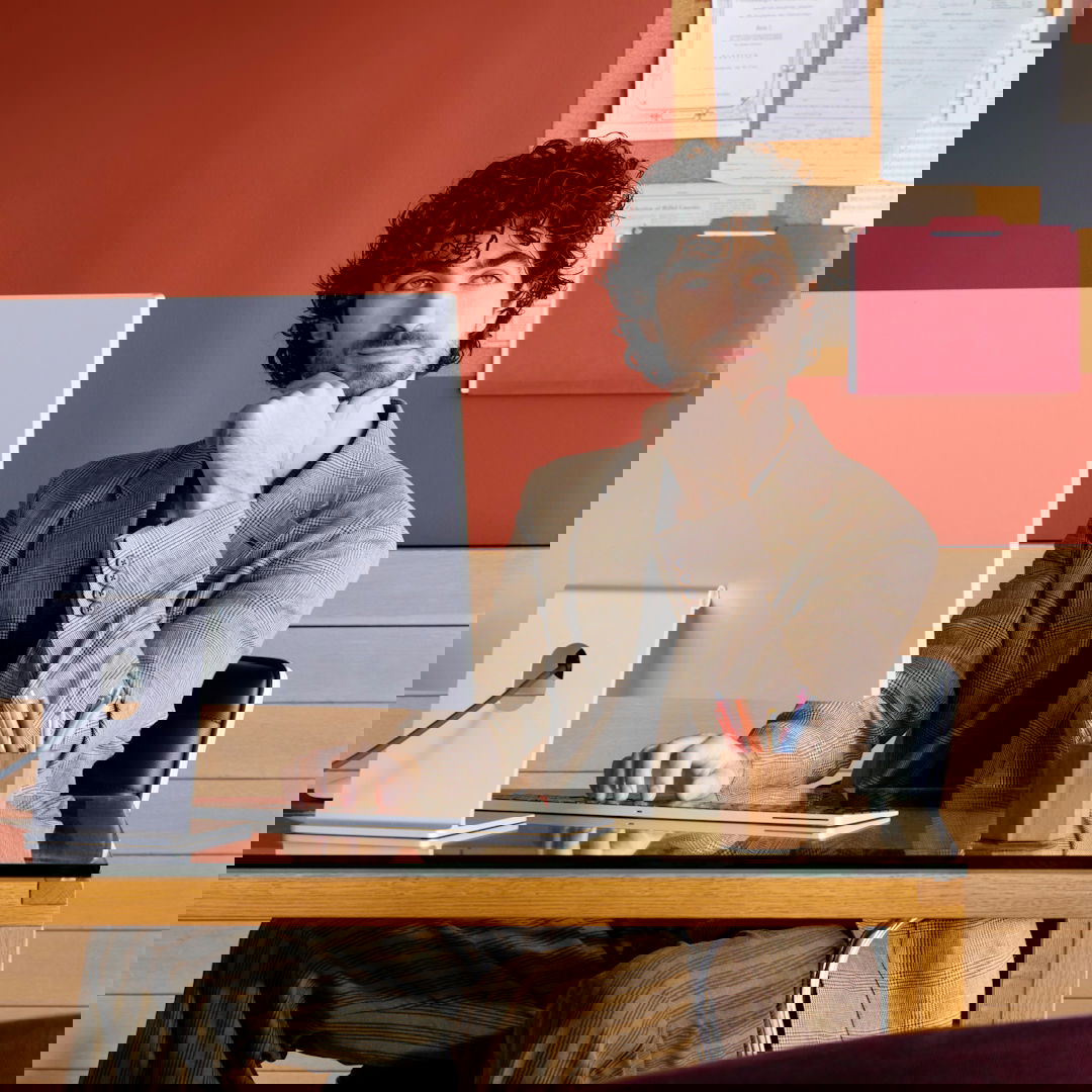 Man sitting at desk with computer, resting chin